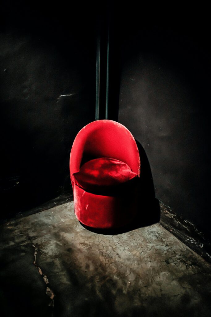 A dramatic red chair in a dark, minimalist corner of a room, highlighting bold modern design.